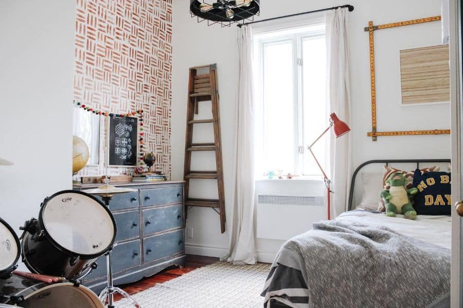 Kids' bedroom with a drum kit, rustic dresser, wooden ladder, and patterned accent wall.