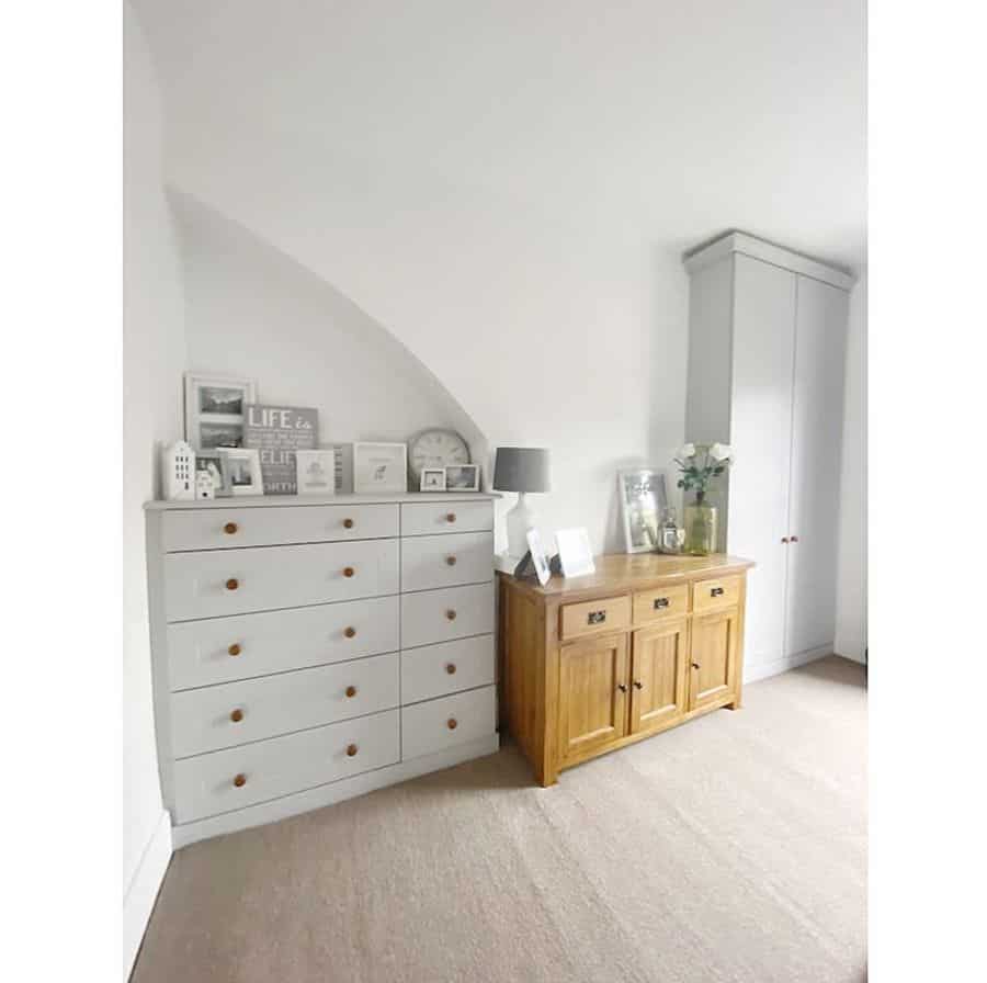 Bedroom with large white dresser, wooden sideboard, and decorative frames.
