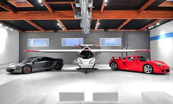 A sleek dream garage featuring luxury cars and a private plane under exposed wooden beams.