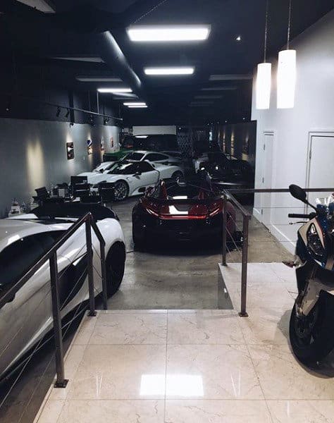 A sleek, dimly lit garage with polished floors showcasing luxury cars and motorcycles in a stylish, modern setting.