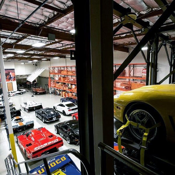A spacious warehouse garage with industrial shelving, lifts, and a vast car collection.
