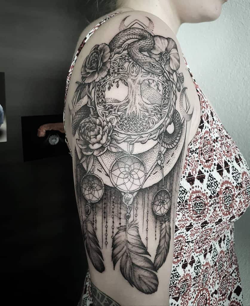 The tattoo blends Yggdrasil with a dreamcatcher, flowers, a serpent, and Celtic knots, symbolizing protection, wisdom, and Norse mythology.