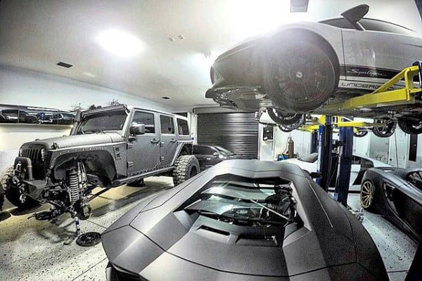 A dream garage equipped with a vehicle lift, featuring a Lamborghini and two rugged Jeeps in a sleek and functional space.