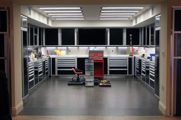 A modern, organized garage with grey cabinets, tool chests, a red stool, and overhead lighting