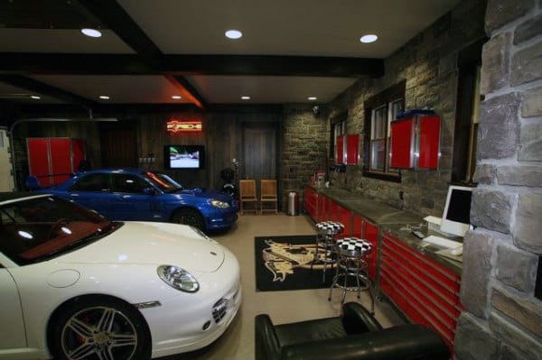 Luxury garage with two cars, brick walls, red cabinets, and a sleek computer on the counter