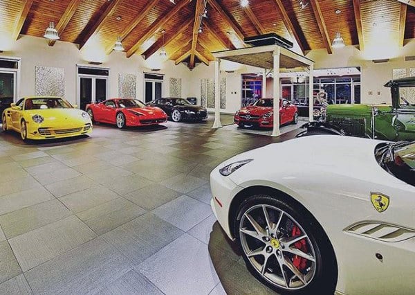A luxury garage featuring high-end cars, tiled flooring, and a vaulted wood ceiling with modern lighting for an upscale and sophisticated display.