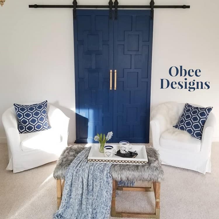 Blue double barn doors with geometric patterns in a modern living room with white armchairs.