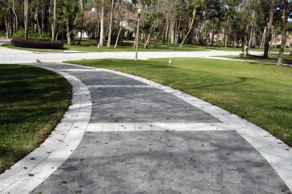 Paver driveway with light stone borders curving through a landscaped yard with trees.