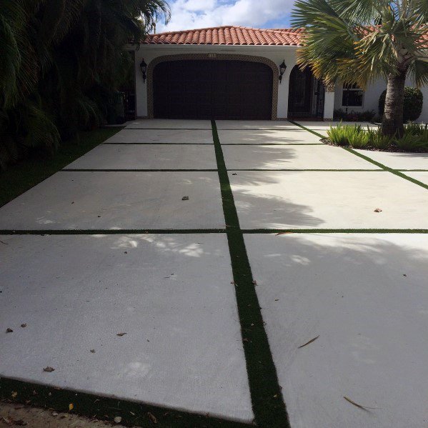 Concrete driveway with grass strips leading to a Mediterranean-style home with a tiled roof.