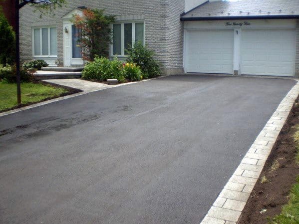 Asphalt driveway with light stone edging leading to a modern house with a double garage.