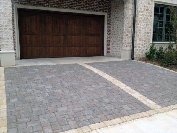 Stone paver driveway with light brick accents leading to a wooden garage door on a brick house.