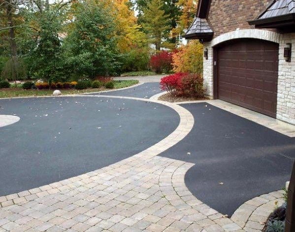 Asphalt driveway with brick edging and a paved walkway near a garage and landscaped garden