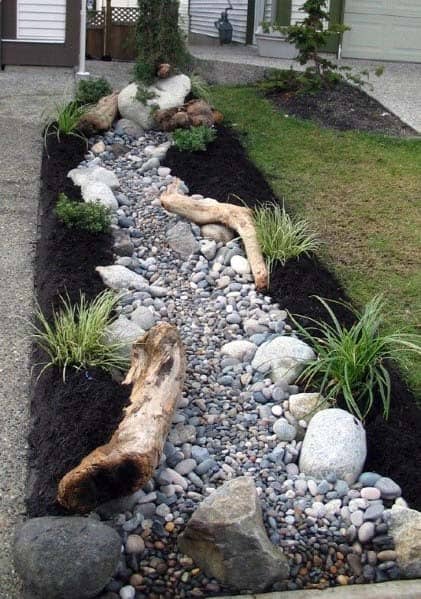 Charming river rock landscaping along a driveway, featuring pebbles, large rocks, and natural wood accents with plants