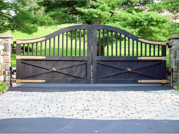 Black wooden driveway gate with arched top, gold hardware, and vertical slats.