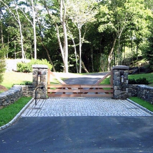 Low-height wooden driveway gate with X-brace design and stone pillar accents.