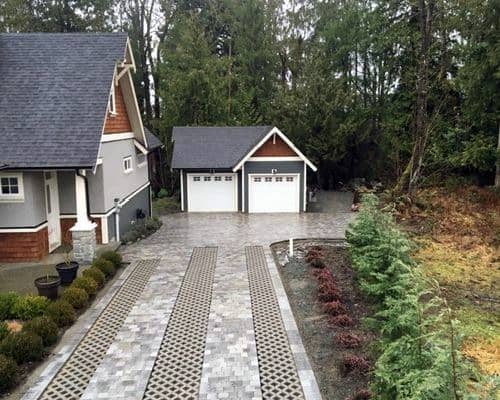 Brick-paved driveway with dual grass-filled permeable strips running down the center.