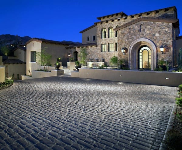 Elegant stone driveway illuminated by soft exterior lighting, highlighting the cobblestone texture and surrounding architecture at dusk