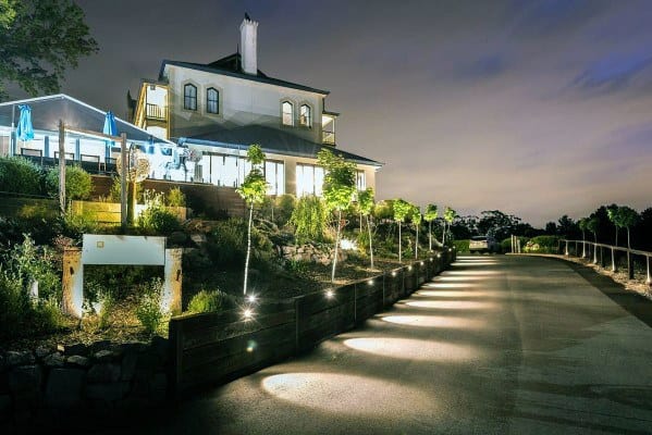 Driveway lined with uplighting along the path, highlighting trees and the surrounding landscaping, creating a welcoming atmosphere at night