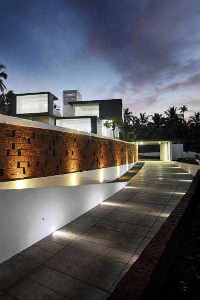 Modern driveway with sleek lighting along a textured wall, casting a warm glow along the path, leading to the entrance at dusk