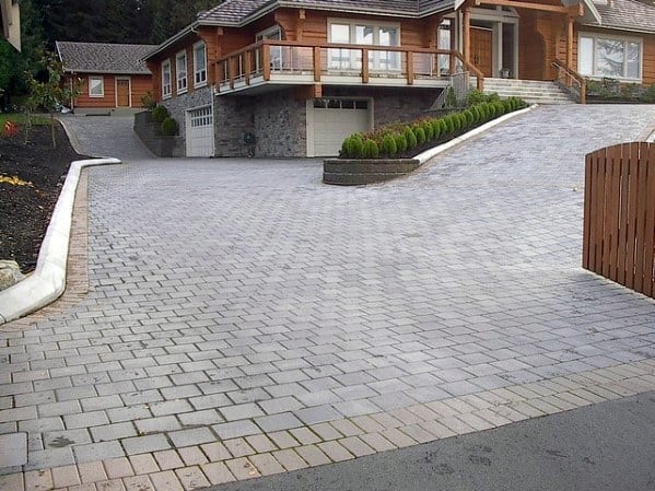 Paved driveway with interlocking gray stones and a gentle slope leading to a wooden house.