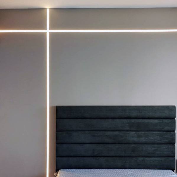 Modern bedroom with minimalist LED strip wall lighting and dark upholstered headboard.