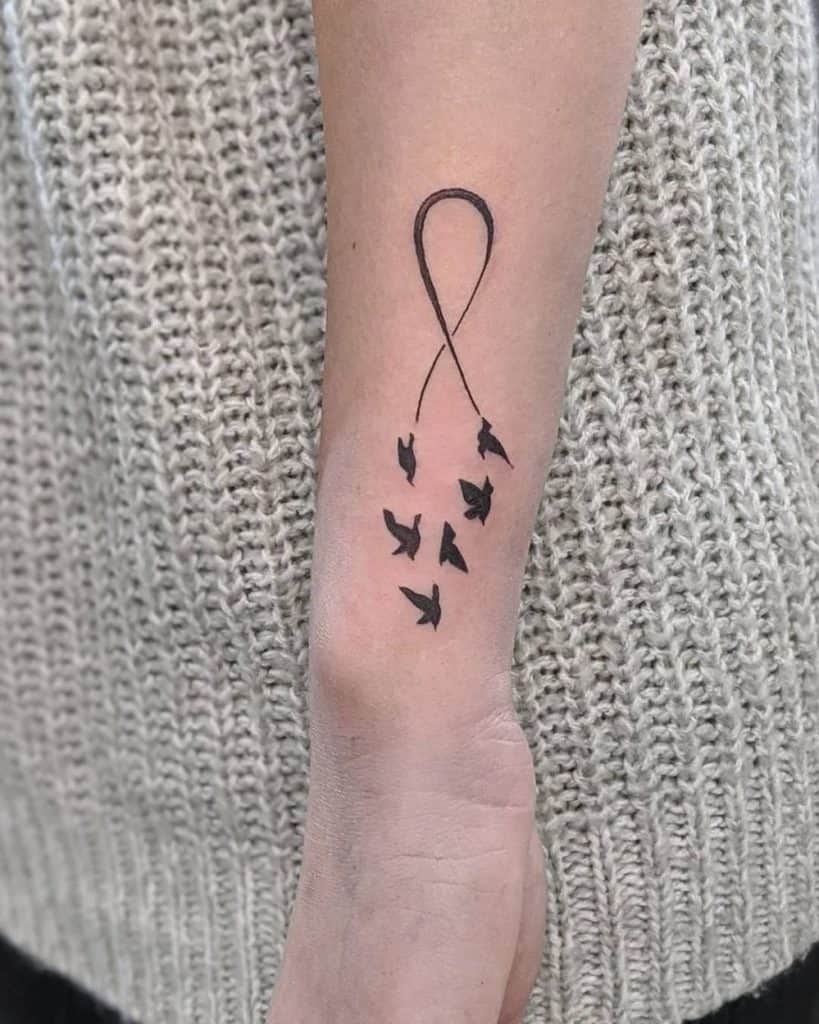 A minimalistic infinity tattoo with birds flying away, creating a sense of freedom and movement.