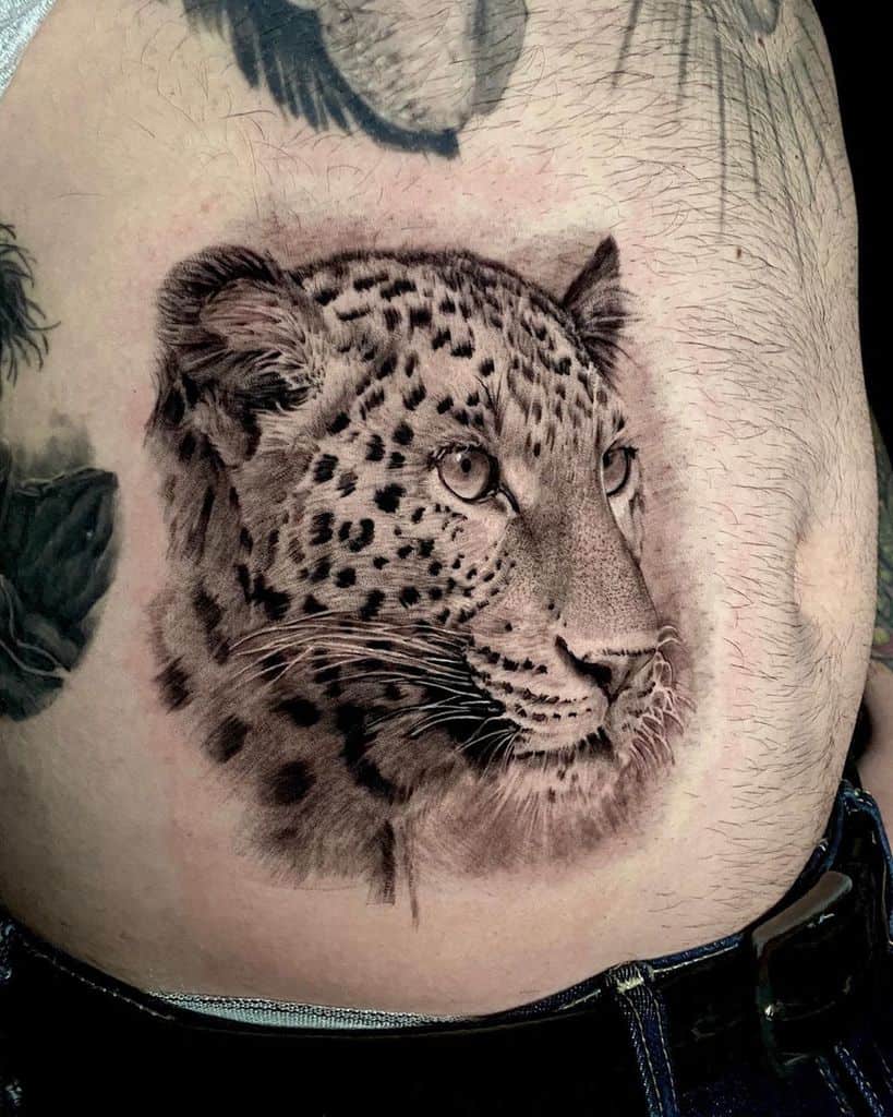 A beautifully detailed black and grey tattoo of a jaguar's face, capturing lifelike shading and textures, placed on the side of the torso.