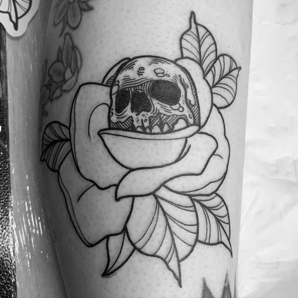 Black ink linework tattoo of a skull emerging from a blooming rose, featuring bold outlines and intricate details on the leg.
