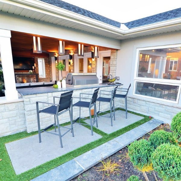 Contemporary outdoor bar with sleek black chairs, stone countertop, and stylish pendant lighting.