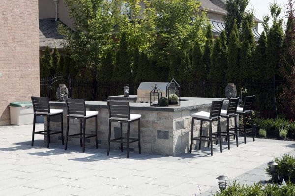 Modern outdoor stone bar with black barstools and lantern decor on a spacious patio.