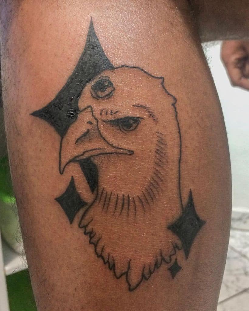 Tattoo of an eagle with a third eye, outlined in black with bold geometric shapes in the background, inked on the thigh.