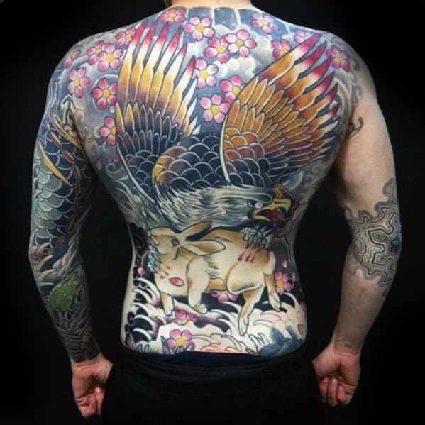 Man with a colorful back tattoo of an eagle catching a rabbit among flowers