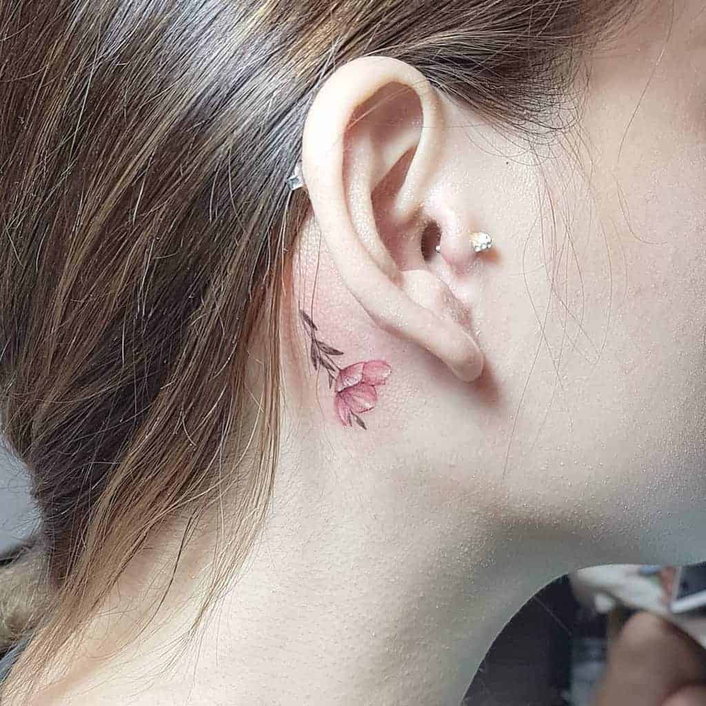 Ear tattoo of pink flowers behind a woman's ear