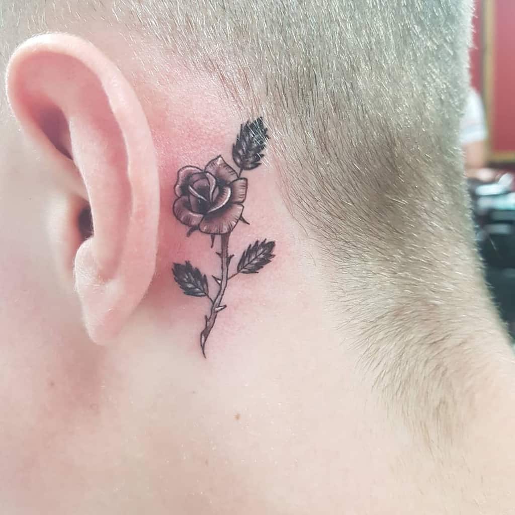A small black rose tattoo behind a person's ear