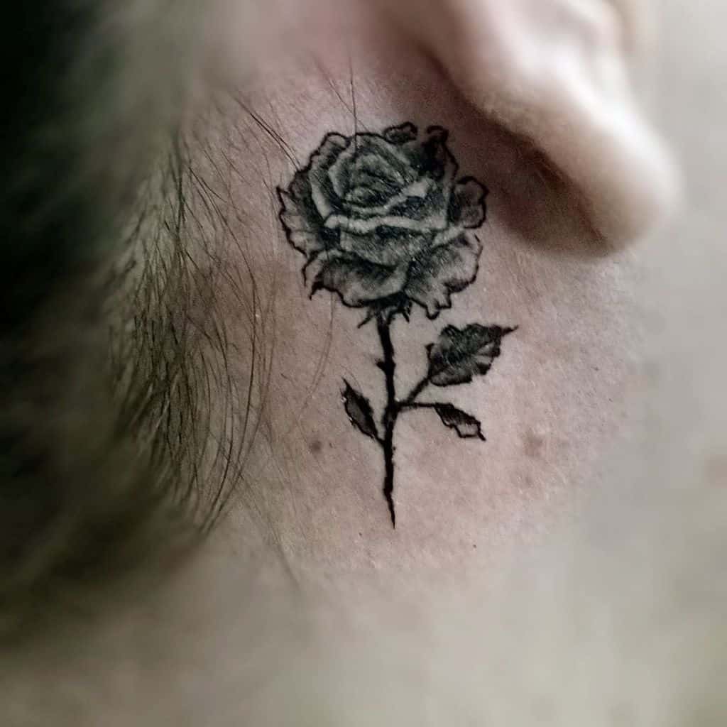 Black rose tattoo behind an ear on skin