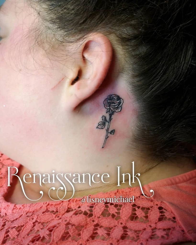 Fine-line black rose tattoo behind the ear, featuring delicate shading and intricate details