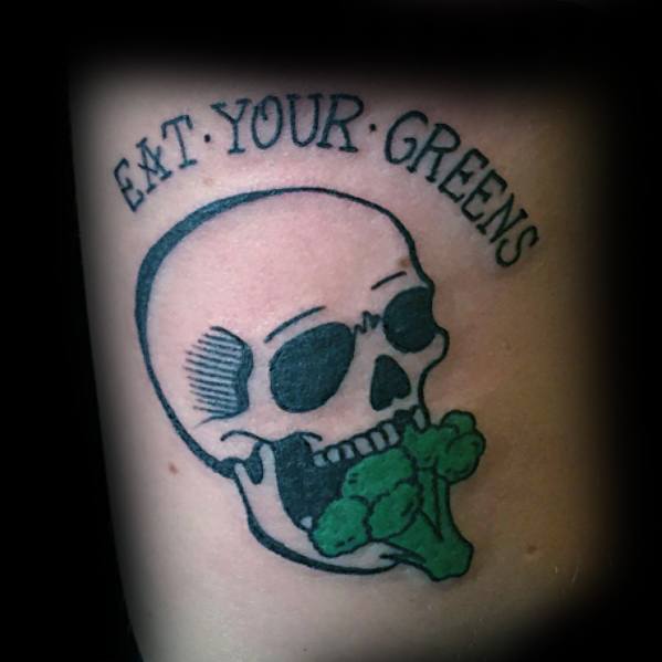 Bold skull and broccoli tattoo with "Eat Your Greens" text, blending dark imagery with a humorous twist in a striking black and green design.