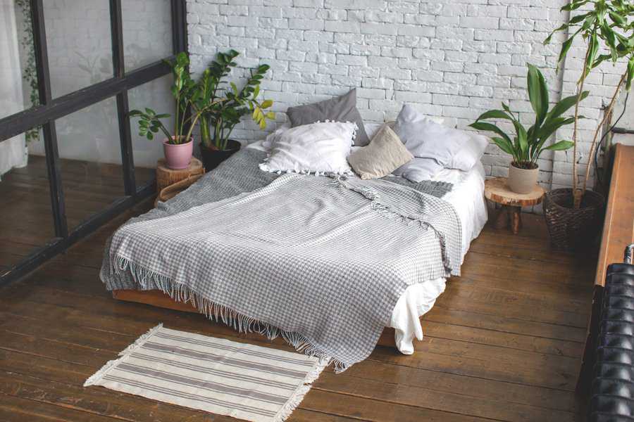 Eclectic bedroom with cozy bedding, potted plants, and a rustic white brick wall.