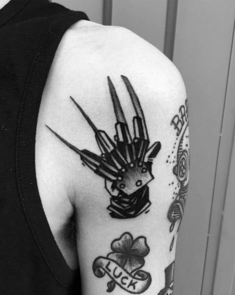 Black and grey tattoo of Freddy Krueger’s glove with sharp blades, placed on the upper arm for a bold and eerie horror design.