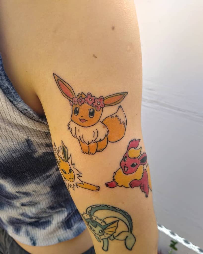 Charming Eevee tattoo with a pink flower crown, joined by Jolteon, Flareon, and Vaporeon for a playful arm design