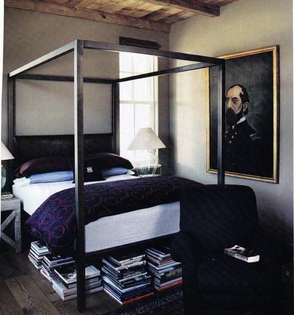 Four-poster bed with stacks of books, portrait on wall, and cozy room decor