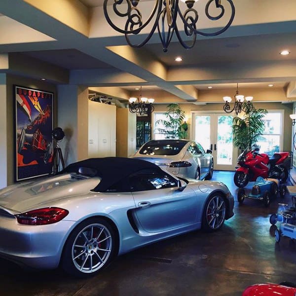 Charming garage with elegant chandeliers, luxury cars, motorcycles, and lush greenery accents.