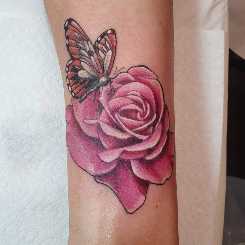 Tattoo of a pink rose with a red and black butterfly resting on the petals, on a forearm
