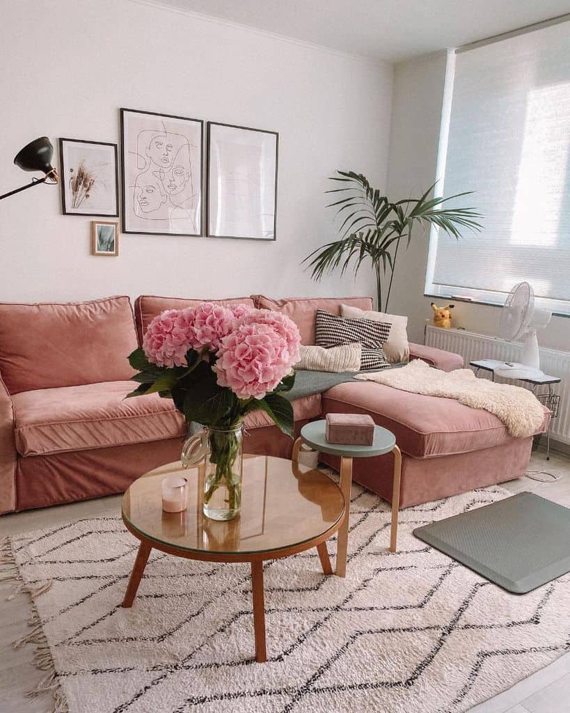 Cozy living room with a pink sofa, plant, coffee table, and wall art, featuring a vase of pink flowers