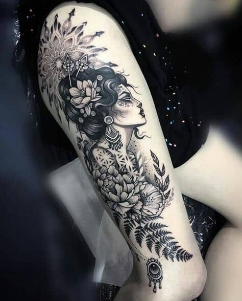 Elegant black and grey tattoo of a gypsy woman with intricate floral and mandala details, flowing hair, and an evil eye charm on the arm.