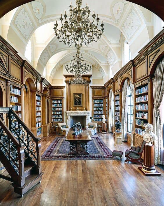 Opulent library with chandeliers, wooden bookshelves, a large table, fireplace, and ornate decor