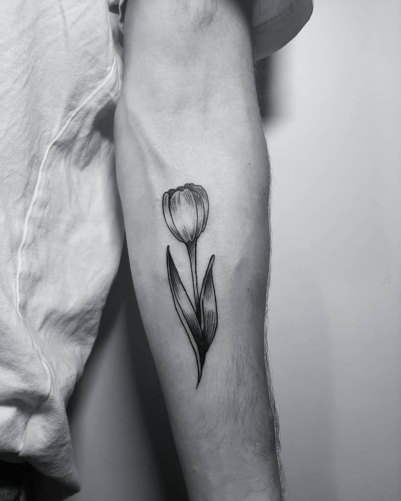 A black and grey tulip tattoo on the forearm, featuring fine linework and shading for a realistic and elegant floral design.
