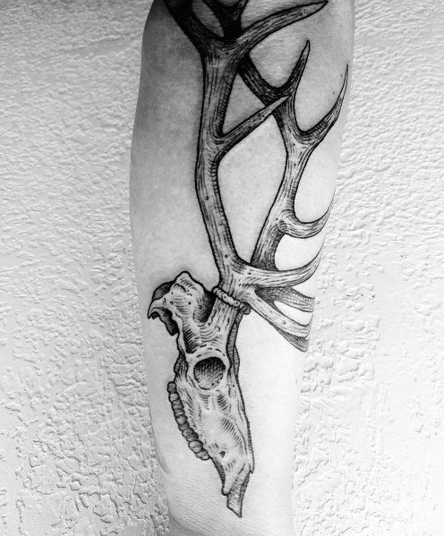 Black and grey elk skull tattoo on the forearm, featuring intricate shading and detailed antlers for a rugged and bold design.