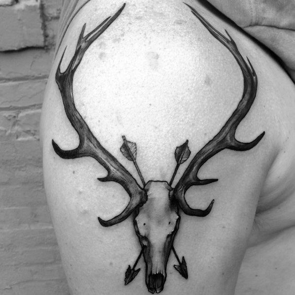 Black and grey elk skull tattoo on the upper arm, featuring detailed antlers and crossed arrows for a bold and rugged design.