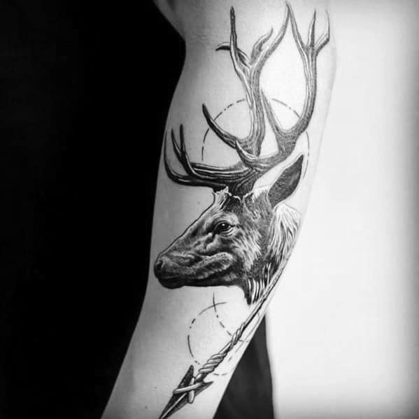 Realistic black and grey elk tattoo on the forearm, featuring intricate antlers, fine shading, and an arrow for a bold and symbolic design.
